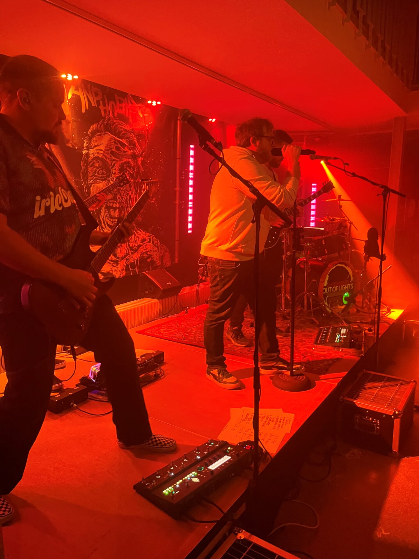 Eine Band bestehend aus drei Personen tritt auf einer kleinen Bühne unter rotem Licht auf.